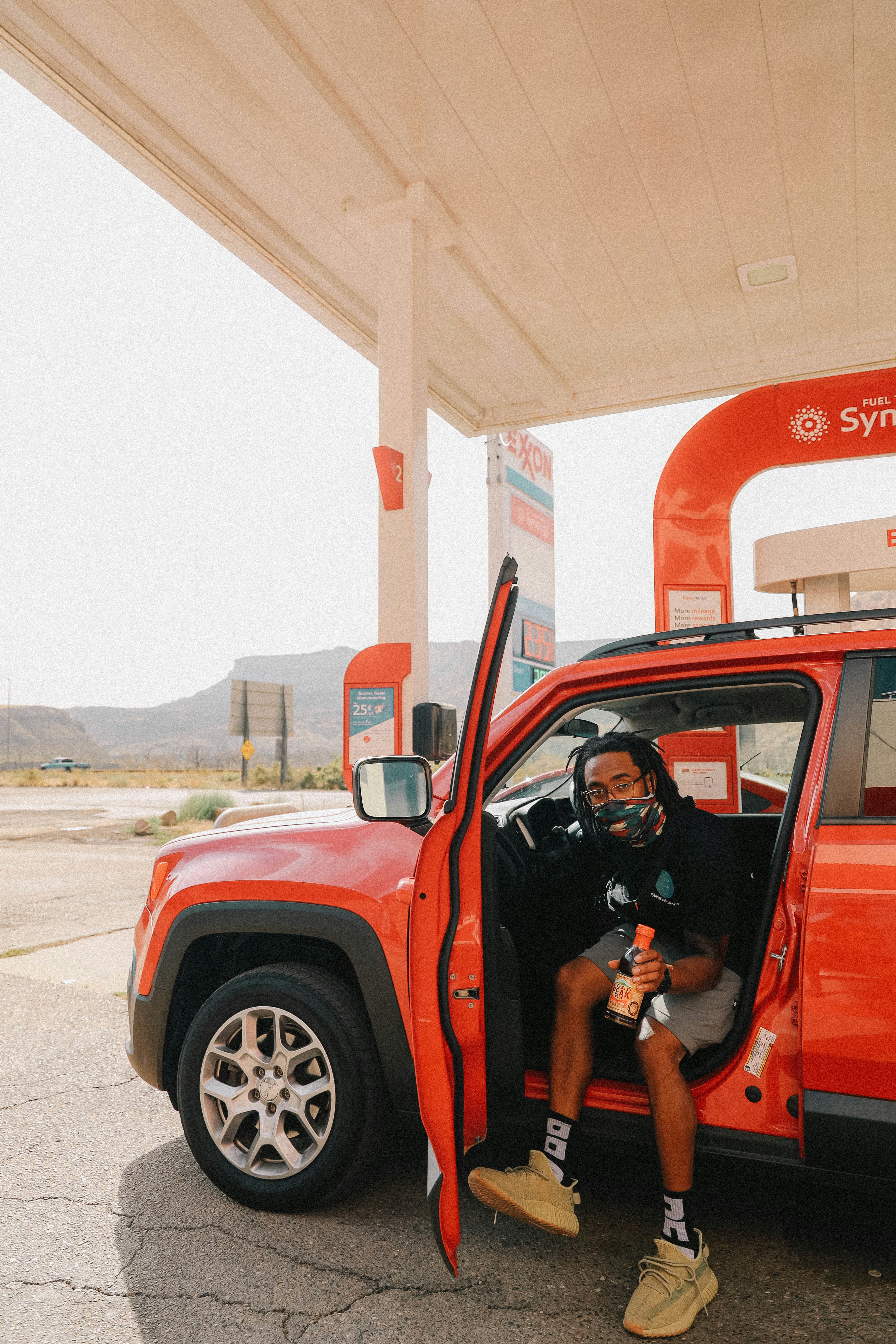 man in black t-shirt and blue denim shorts standing beside red suv during daytime